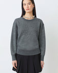 Woman wearing a gray sweater and black pleated skirt on a white background