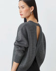 Woman wearing a gray open-back sweater against a white background