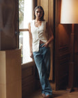Woman wearing The Tommy Low Slung Straight standing in a room with wooden paneling and a lamp.