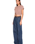A model wearing a dusty rose short-sleeve crop top and high-waisted, wide-leg blue jeans with a brown belt, standing against a solid white background.