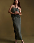 A woman modeling a dark olive green sleeveless maxi dress with lace trim at the bust and along the side, paired with black strappy heels, against a solid dark olive background.