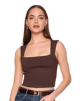 A woman modeling a dark brown square-neck crop top with wide straps, paired with blue jeans and a brown belt, against a solid white background.