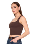 A woman modeling a dark brown square-neck crop top with wide shoulder straps, paired with blue jeans, against a solid white background. Side view