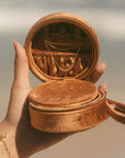 Brown round velvet jewelry box held by a hand with a blurred background
