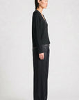 model wearing a black vneck sweater over a silky black top with black pants on a grey background, side view