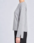 model wearing a grey long sleeve sweater and black pants on a grey background, side view