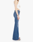 Woman wearing blue flared jeans and a white top on a white background, side