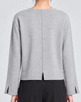 model wearing a grey long sleeve sweater and black pants on a grey background, back view with back vent slit and wrist