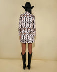 Person wearing a patterned outfit, black boots, and a cowboy hat on a beige background. back view