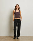 Woman wearing a brown tank top and black pants against a plain background front view