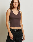 Woman wearing a brown tank top and black pants against a plain background front view