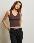 Woman wearing a brown tank top and black pants against a plain background front view