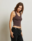 Woman wearing a brown tank top and black pants against a plain background side view
