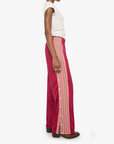 A model shown in profile wearing a white sleeveless top and high-waisted, wide-leg magenta trousers with vertical pink and white stripes down the sides, set against a plain light gray background.