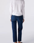 A person shown from the back wearing a white long-sleeve top, dark blue straight-leg jeans, and black flats, photographed against a light gray studio background.