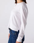 Person wearing a white long-sleeve shirt and blue jeans on a plain background