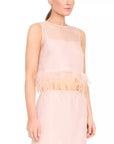 A woman wearing a sleeveless pale blush pink dress with a sheer mesh yoke and a ruffled tulle waistband, shown against a plain white studio background.