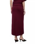 A woman wearing a long, dark burgundy maxi skirt with a matching top and black pointed-toe mule heels, shown from the back against a plain white background.