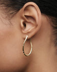Gold hoop earring worn on an ear with a blurred background