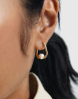 Gold hoop earring with a pearl on an ear against a neutral background