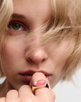 Close-up of a person wearing a gold ring with pink stone on a neutral background