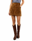 model wearing saddle mini skirt with gold studs and boots on a white background