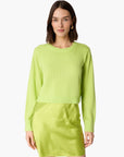 A woman modeling a bright lime green cropped long-sleeve sweater and a matching mini skirt, set against a plain white studio background.