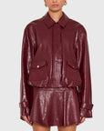 A model wearing a glossy burgundy faux-leather jacket and matching mini skirt set against a light gray studio background.