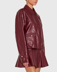 A woman wearing a glossy burgundy faux-leather jacket and matching mini skirt against a light gray studio background.