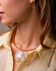 Close-up of a woman wearing gold hoop earrings and a gold necklace with a pearl pendant.