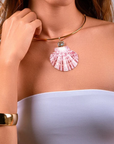 A close-up of a model wearing a gold-tone choker necklace with a pink and white seashell pendant and a small blue stone accent.