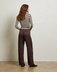 Woman wearing a striped sweater and brown pants against a plain background back view