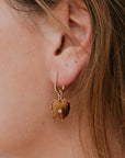 Close-up of a person wearing a gold earring with a brown stone.