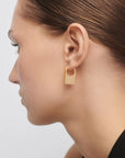 Gold hoop earring worn by a person on a light gray background