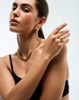 Woman wearing gold jewelry including earrings, necklace, and ring on a white background