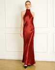 Woman wearing a red satin halter neck gown against a white wall.
