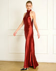 Woman wearing a red halter neck gown against a white wall, side view