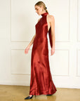 Woman wearing a red satin halter neck gown against a white wall, side/front
