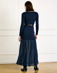 Woman wearing a navy blue dress with a belt against a white wall.