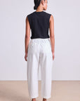 Person wearing a black sleeveless top and white pants on a plain background, back view