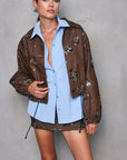 Woman wearing a brown floral jacket over a light blue shirt against a gray background