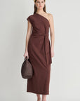 model wearing a one shoulder brown dress with a white background