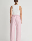 Person wearing a white sleeveless top and pink pants on a light gray background