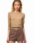 Woman wearing a beige long-sleeve top and brown shorts with a belt on a white background