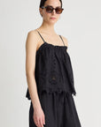 Woman wearing a black sleeveless top with floral embroidery on a plain background