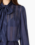 close up of a model wearing a sheer navy top with a tie neck