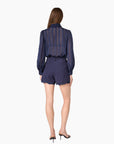 model wearing a navy sheer top with a tie neck with navy shorts that lace a small lace trim on a white background, back view