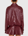 A person shown from the back wearing a glossy burgundy faux-leather jacket with a collar, long sleeves, and a gathered waist with a matching peplum-like flared section, against a light gray studio background.