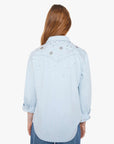 Woman wearing a light blue denim shirt with floral embroidery on a white background