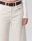 Person wearing white pants with a brown belt and white shirt on a light gray background